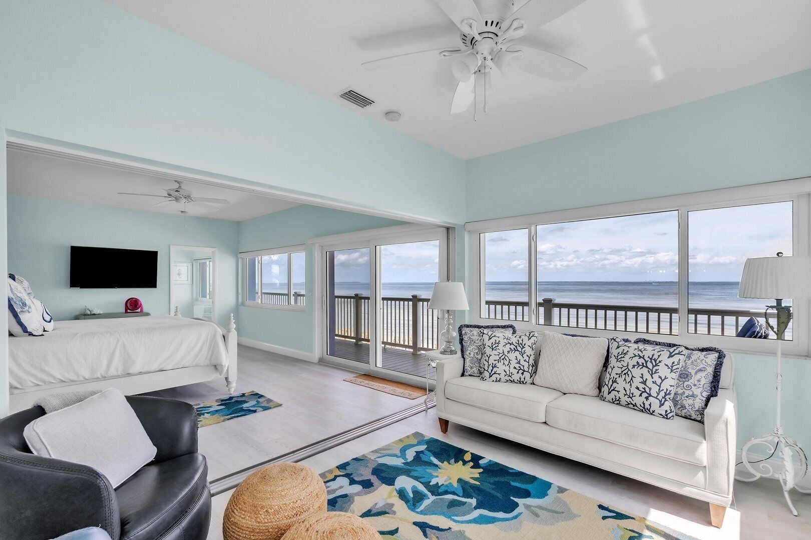 A spacious room with a bed, a sofa, and a large window offering a view of the ocean.