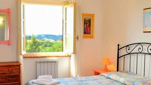 Une chambre à coucher comprenant un lit, une commode, une fenêtre donnant sur un paysage agréable, un radiateur et une lampe.