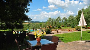 Une terrasse extérieure aménagée avec des meubles en osier, une table en verre et une vue sur une piscine et un jardin paysager.