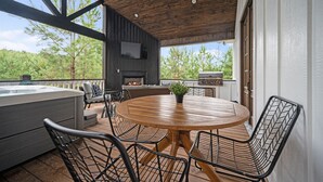 An outdoor patio with a round wooden table and metal chairs, a hot tub, and a grill area.