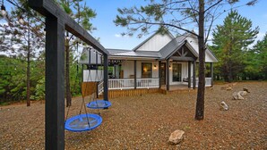 A cabin with a deck, surrounded by trees and a gravel ground.
