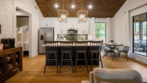 A modern kitchen with white cabinets, a central island with bar stools, and a wooden ceiling.