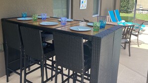 En uteservering med ett långt bord, svarta flätade stolar och blått glas.