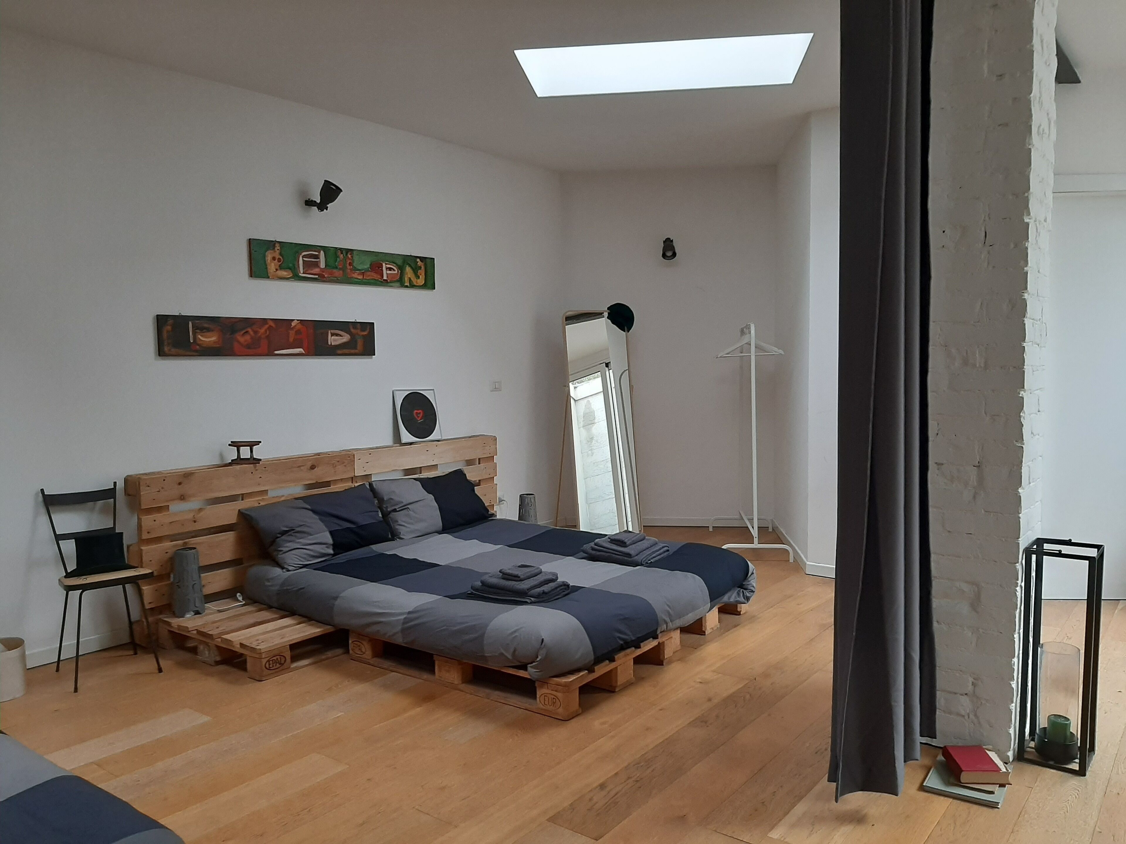 Une chambre à coucher avec un cadre de lit en bois, deux lits, une petite table, une chaise, un miroir et une lampe sur pied.