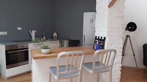Une cuisine compacte avec un îlot central en bois, des chaises blanches et un mur d’accent en briques blanches.