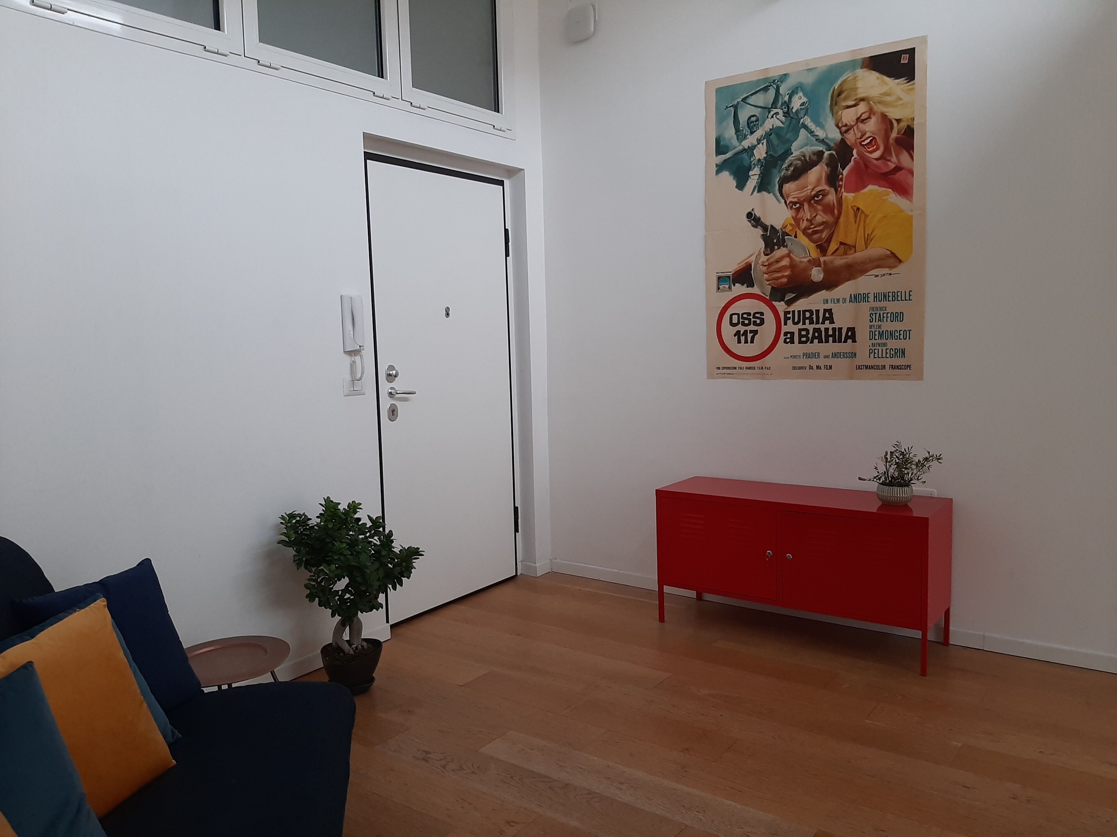 Una habitación con una puerta blanca, un armario rojo, una planta en maceta y un cartel en la pared.