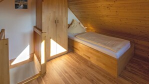 A small, cozy room with a wooden bunk bed, a wardrobe, and a sloped ceiling.
