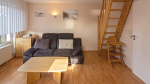 A cozy living room with a wooden floor, a dark grey sofa, a wooden coffee table, a wooden ladder, and a small cabinet with a radio.