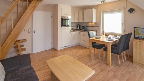 A compact living space with a wooden staircase, a kitchenette, a dining area with a table and chairs, and a sofa.