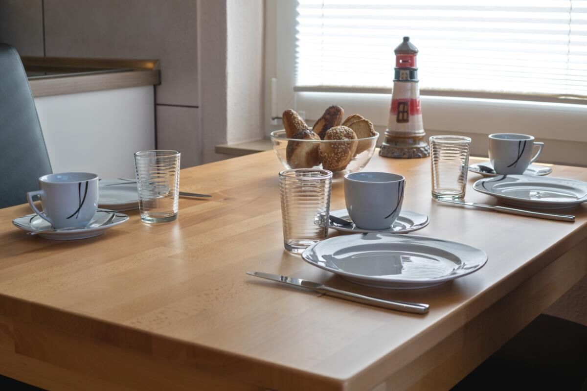 Una mesa de comedor dispuesta con platos, tazas y un bol de galletas.