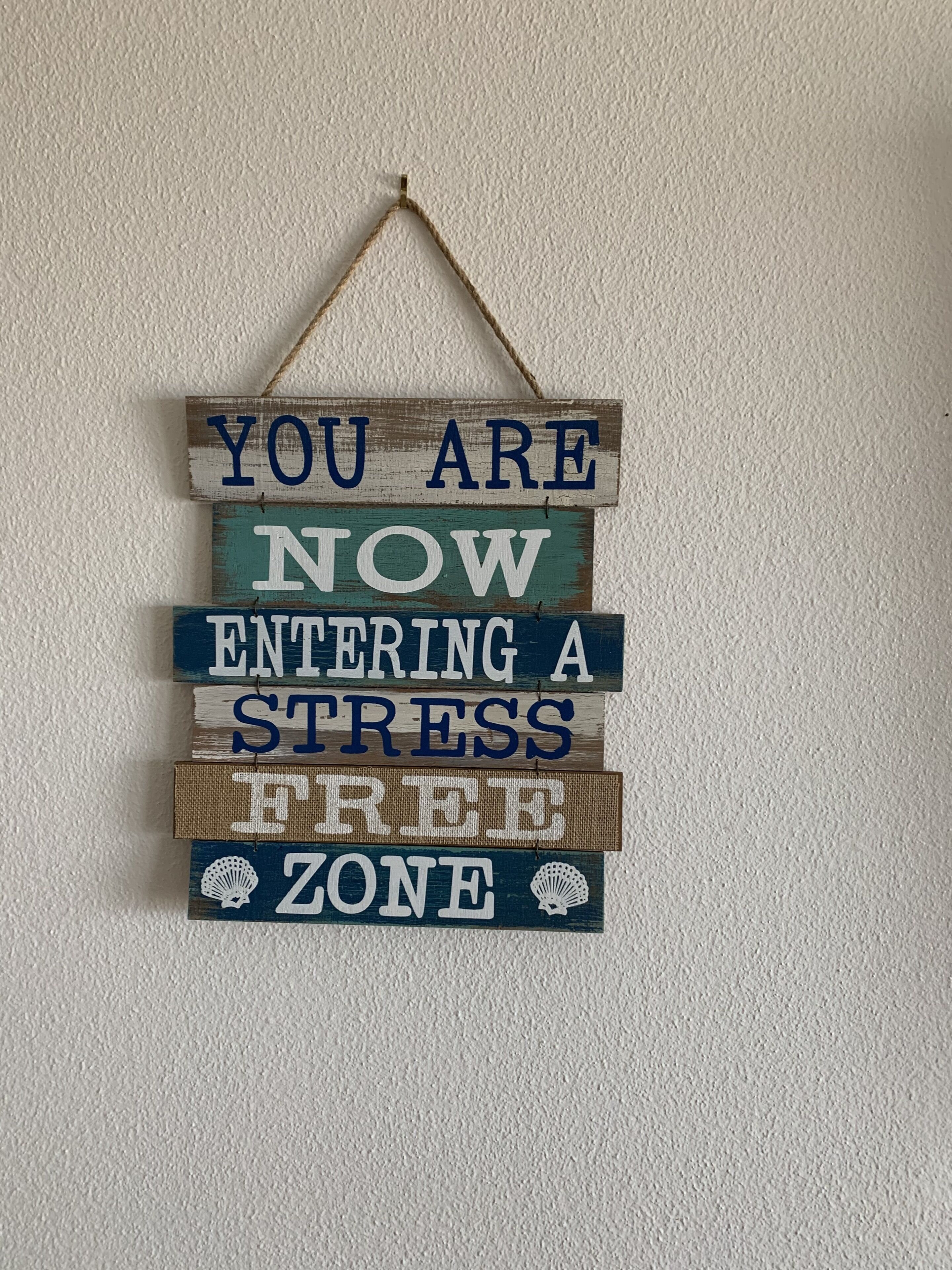 A wooden sign with the text "YOU ARE NOW ENTERING A STRESS FREE ZONE" hanging on a wall.