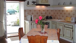 A dining area with a table set for four, a vase with flowers, and a kitchen in the background. - Les Gîtes de Garz Ar Bik Gîte for 2/3 people (Brasparts)