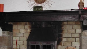 A fireplace with a brick surround, a decorative sunburst above it, and a basket of firewood on the mantel. - Les Gîtes de Garz Ar Bik Gîte for 2/3 people (Brasparts)