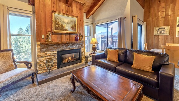 A cozy living room with a fireplace, leather sofa, and a large window offering a mountain view. - 1 + Loft w/ Views Next to the Village at Mammoth! (Mammoth Lakes)