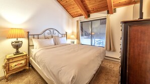 A bedroom with a wooden ceiling, a bed with white bedding, a nightstand with a lamp, and a window with curtains. - 1 + Loft w/ Views Next to the Village at Mammoth! (Mammoth Lakes)