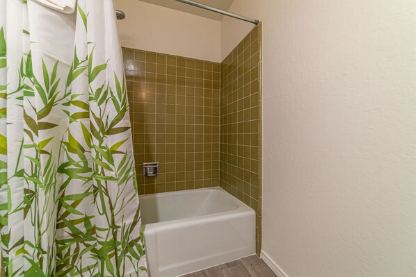 A bathroom with a white bathtub, green-tiled walls, and a bamboo-patterned shower curtain.