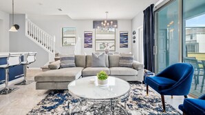 A modern living room with a grey sofa, a round coffee table, and a blue chair. There is a staircase with white railings leading to another level.