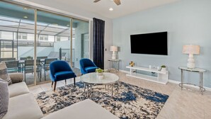 A modern living room with a ceiling fan, a flat-screen TV, a glass partition, and a dining area with chairs and a table.
