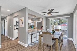 Une cuisine moderne avec un coin bar, une table à manger avec des chaises et un ventilateur de plafond.