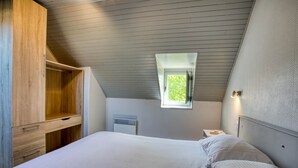 Une chambre avec un plafond en pente, une fenêtre, un lit avec une literie blanche et une armoire en bois.