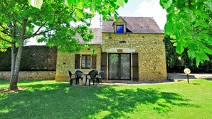Un bâtiment en pierre doté d’un petit porche et d’une table avec des chaises.