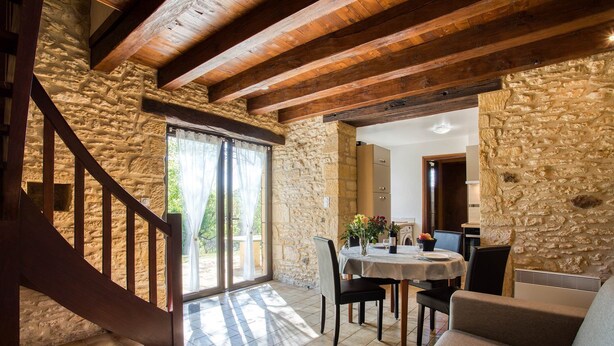 Un vaste espace de vie agrémenté d’un mur en pierre, de poutres apparentes, d’une table à manger avec des chaises et d’un canapé.