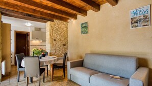 Une pièce chaleureuse avec un mur en pierre, un plafond en bois, un canapé gris et une table à manger avec des chaises.