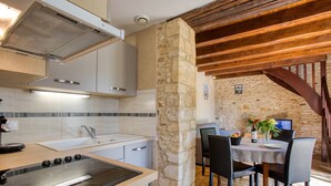 Une cuisine avec une colonne en pierre, des poutres en bois et un coin repas comprenant une table et des chaises.