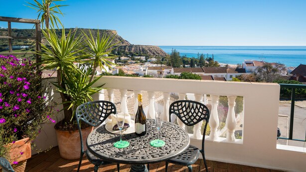 Ein Balkon mit Tisch und Stühlen mit Blick auf eine Küstenstadt und das Meer.