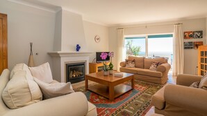 Ein Wohnzimmer mit Kamin, einer Couch, einem Couchtisch mit Pflanze und Meerblick durch große Fenster.