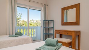 Ein Hotelzimmer mit zwei Betten, einem Holfnachtkästchen, einem Spiegel und einem Fenster mit Vorhängen.