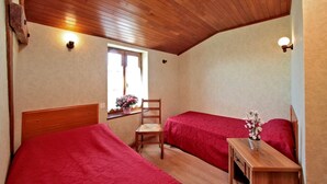 Un dormitorio con dos camas, cabeceros de madera, una mesita de noche de madera, una silla y una ventana con vistas.