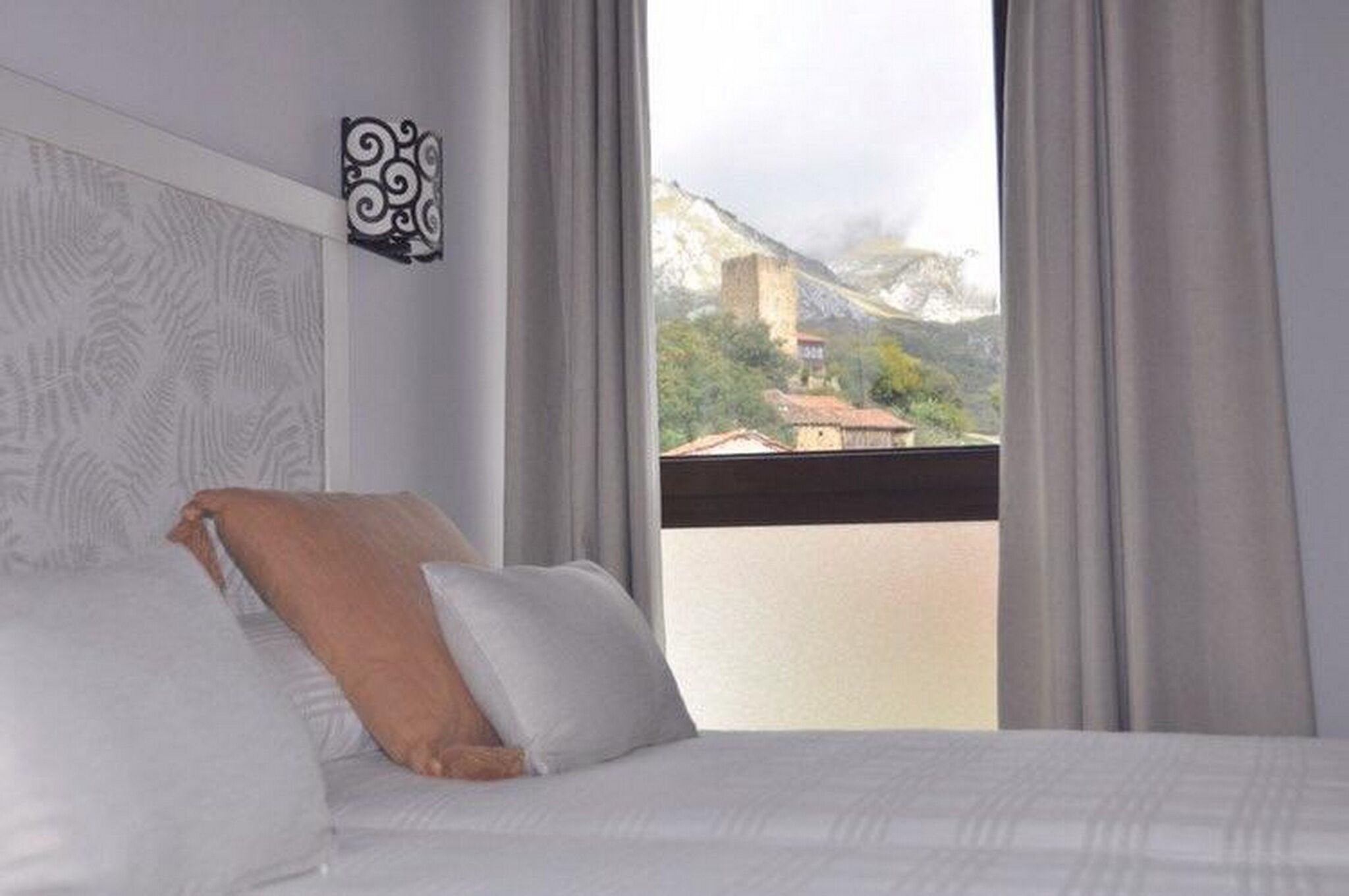 A hotel room with a bed, a view of a mountain and buildings, and a decorative wall piece.