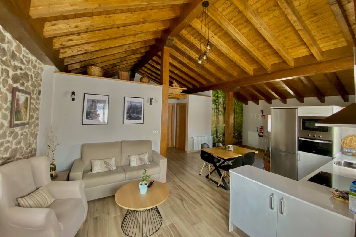 A cozy interior with a wooden ceiling, a sofa, a dining table, and a kitchen area.