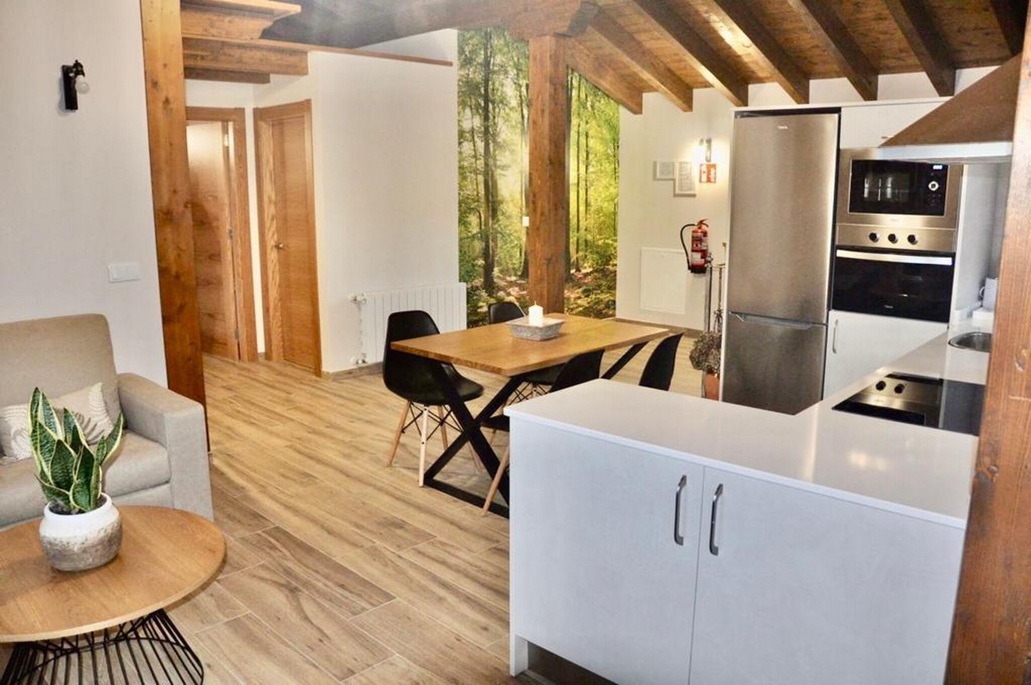 A modern kitchen with a built-in oven and microwave, a dining area with a wooden table and chairs, and a cozy seating area with a sofa and a potted plant.