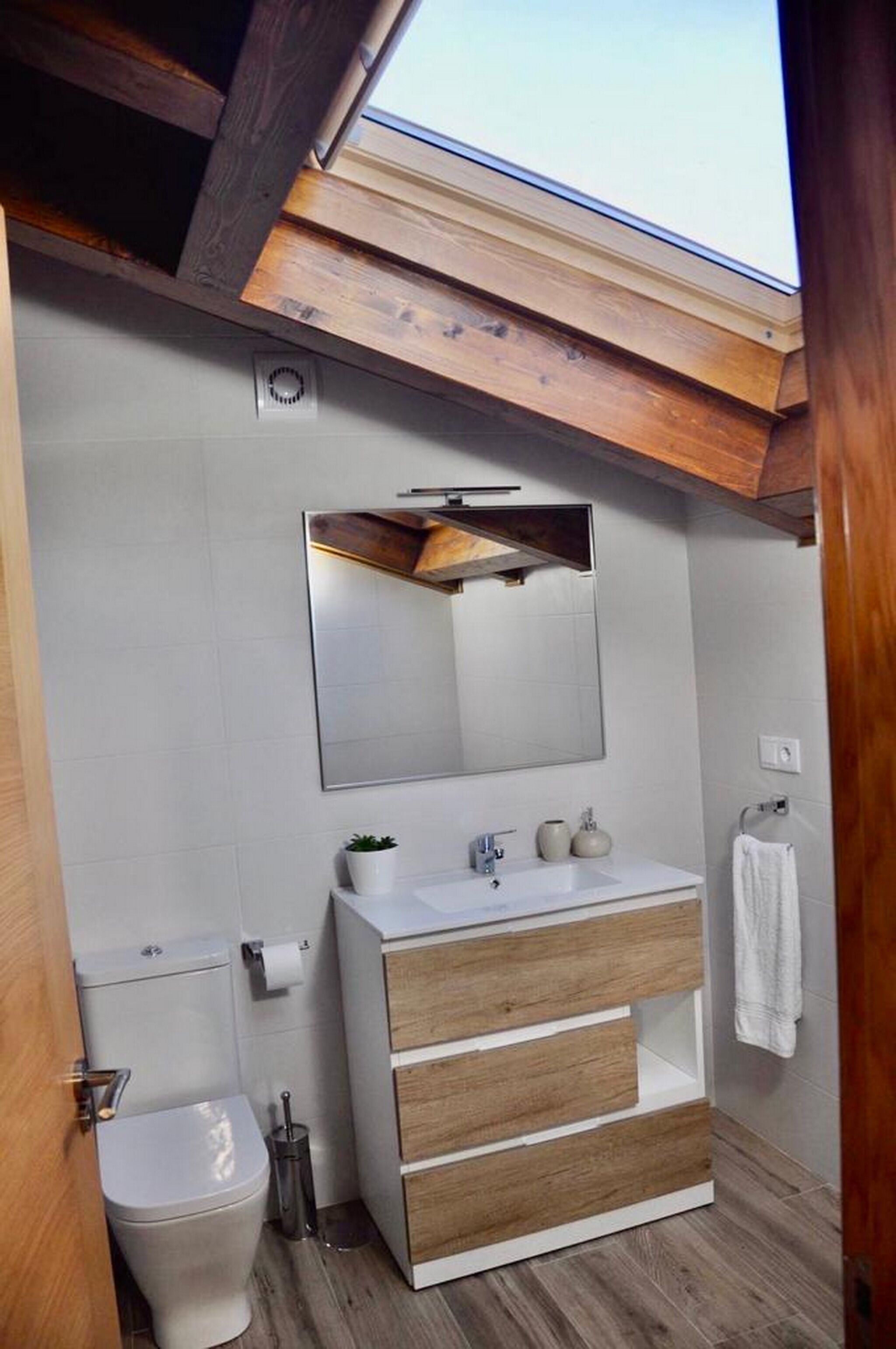 Et moderne badeværelse med ovenlys, et stort spejl, en trækommode og et toilet.