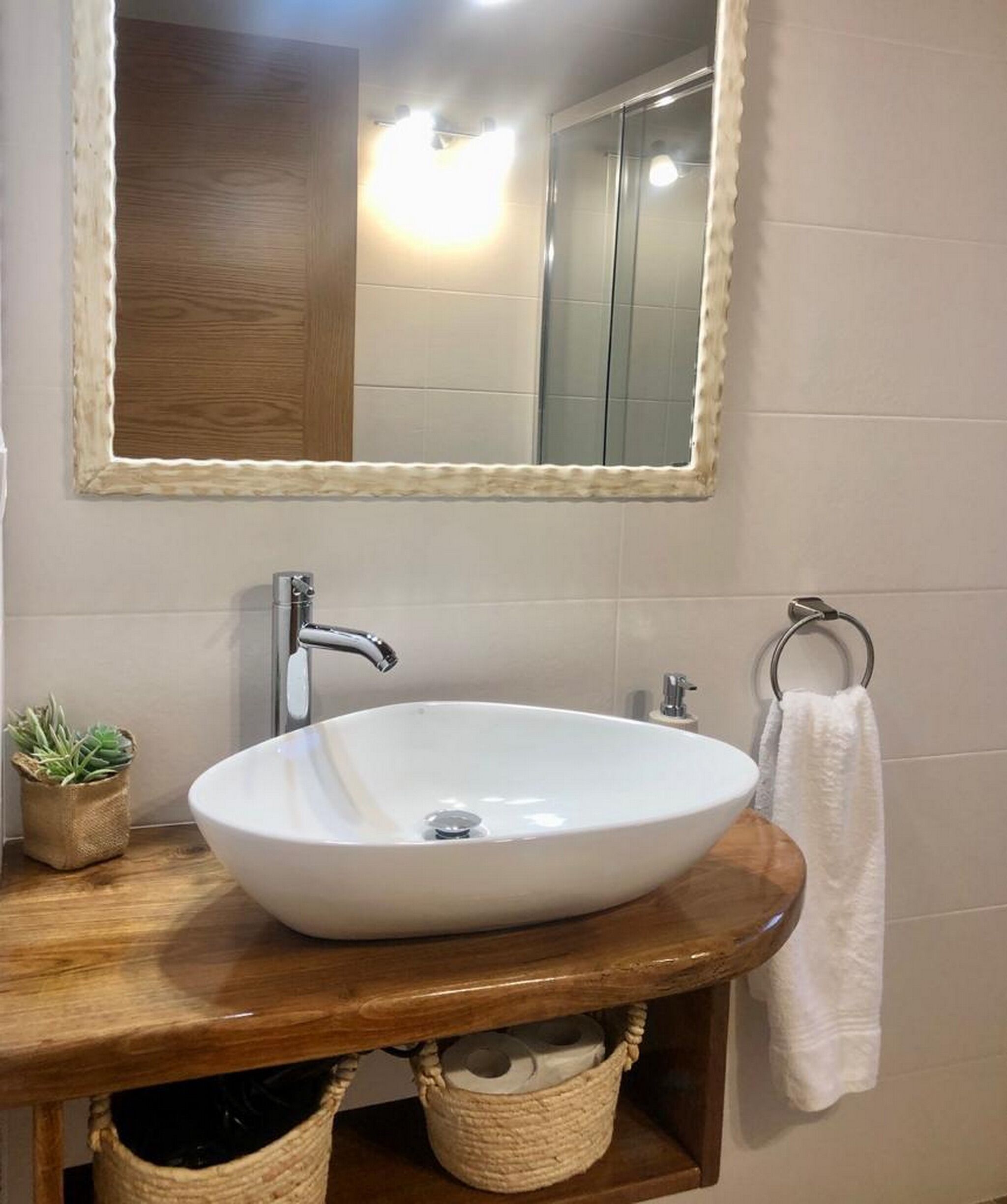 A bathroom with a white sink, wooden vanity, a mirror, and a towel rack.