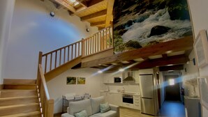 A spacious living area with a staircase leading to an upper level, a kitchen with modern appliances, and a large mural of a waterfall. - Apartamentos la Ventana de Mogrovejo (Camaleno)