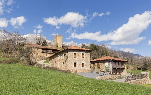 A stone building with a red-tiled roof, a balcony, and a stone tower. - Apartamentos la Ventana de Mogrovejo (Camaleno)