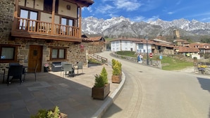 A traditional stone building with a balcony, outdoor seating, and a view of snow-capped mountains. - Apartamentos la Ventana de Mogrovejo (Camaleno)