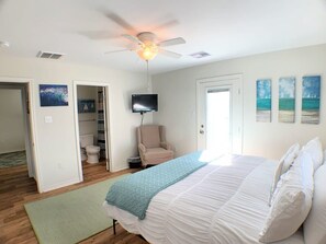 Une chambre à coucher avec un lit, un ventilateur de plafond, une télévision et des œuvres d’art accrochées aux murs.