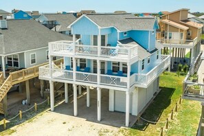 Une maison à plusieurs étages située en bord de mer, dotée d’un balcon, d’une terrasse couverte et d’un escalier menant à l’étage supérieur.