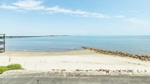 A beach with a pier extending into the water, a sandy shore, and a concrete structure on the left. - Annie by the Sea - Oceanfront, Sunrise & Sunset Decks! (Freeport)