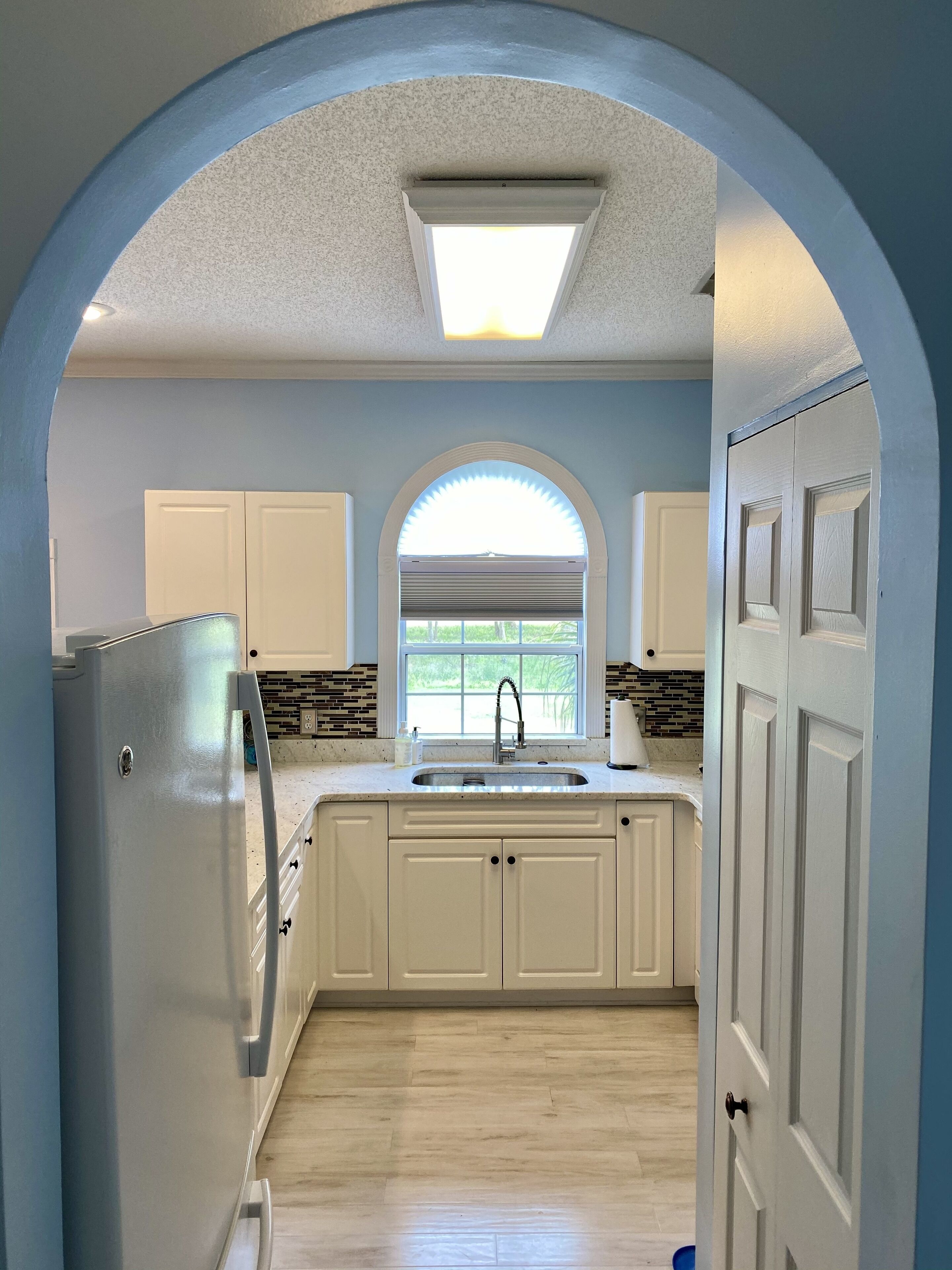 A kitchen with white cabinets, a built-in sink, and a window with a view of greenery.