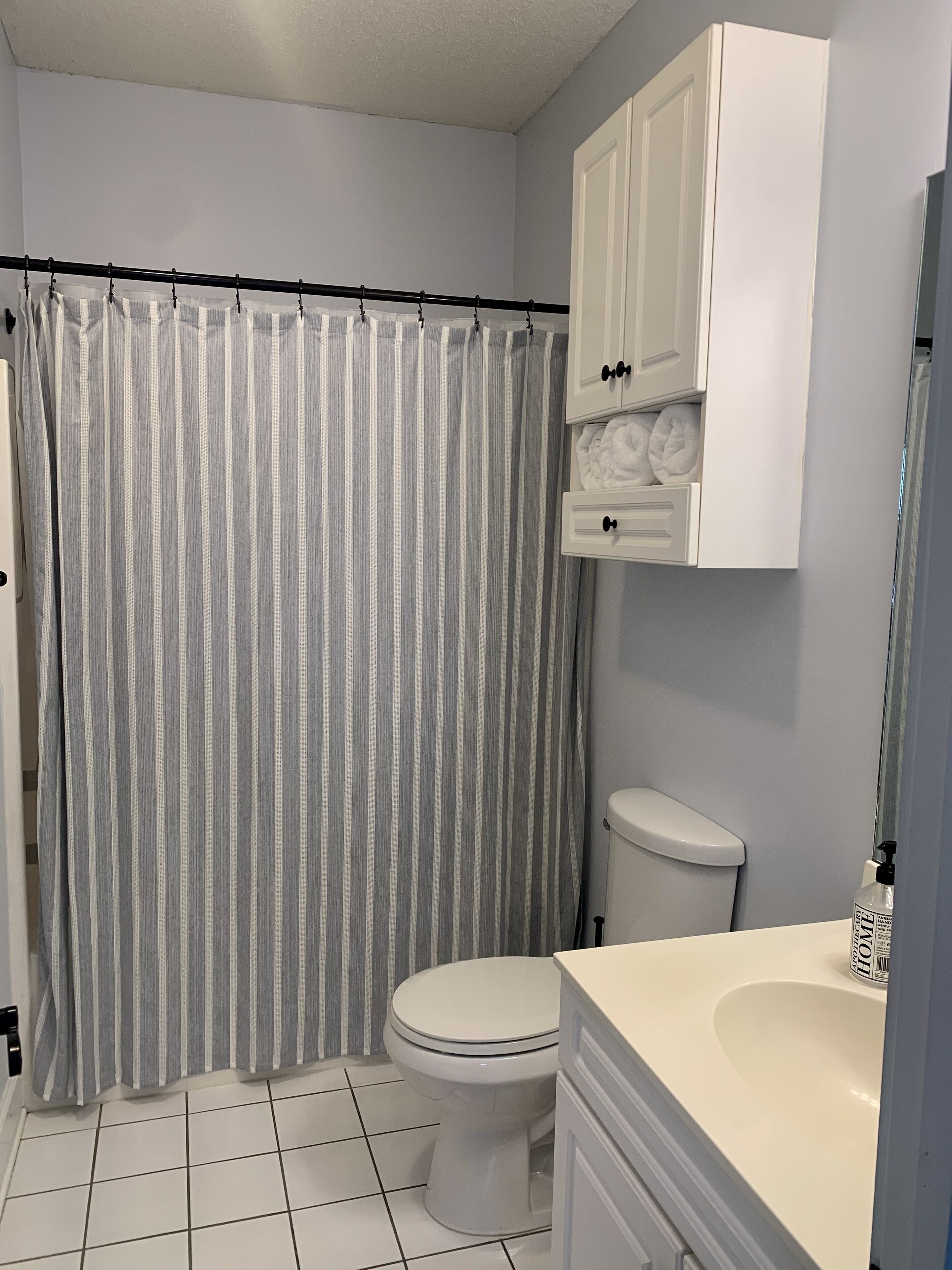 Een badkamer met een gestreept douchegordijn, toilet, wastafel en een kastje boven de wastafel.