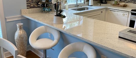 A kitchen with white cabinets, a large island with bar stools, a window with blinds, and a backsplash with a mosaic tile pattern.