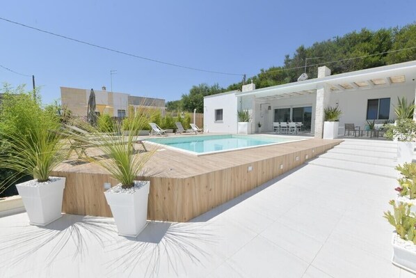 A modern outdoor pool area with a wooden deck, lounge chairs, and potted plants. - Il Marchese in Piscina (San Pietro In Bevagna)