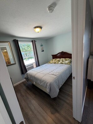 Quarto com cama, luminária no teto, janela com cortinas e porta.