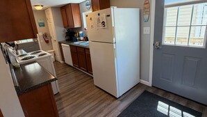 Una cocina compacta con armarios de madera, un refrigerador blanco, una estufa y un felpudo negro.