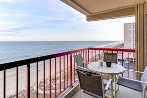 A balcony with a table and chairs overlooking a beach and ocean.